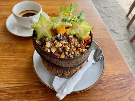 A smoothie bowl with fresh tropical fruit and granola topped with starfruit and a side of coffee on a wooden table.