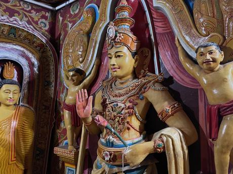 Detailed, brightly colored statues of deities inside a temple, with intricate floral patterns decorating the walls.