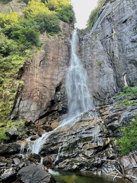 A tall waterfall cascading down a rocky cliff with lush green vegetation at the top and a small pool of water at the bottom.