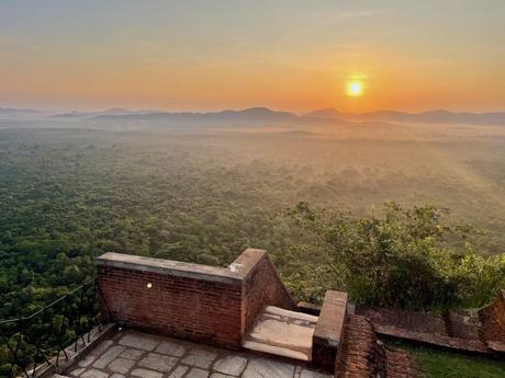 A breathtaking view of a golden sunrise over a vast forest landscape, seen from the top of Sigiriya Lion's Rock.