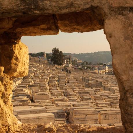 A stone-framed view of a large cemetery in Jerusalem on the Mount of Olives, with rows of tightly packed, traditional stone graves stretching into the distance.