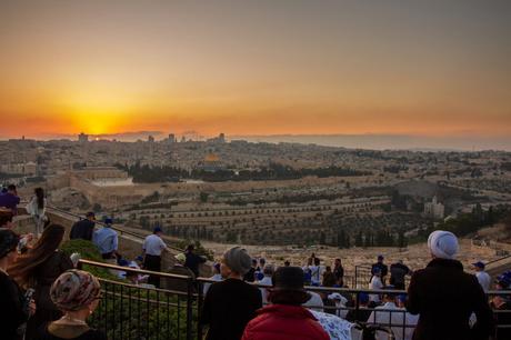 A group of people gathered on a scenic overlook at sunset, with a panoramic view of Jerusalem’s Old City, featuring the golden Dome of the Rock and ancient stone walls in the distance.