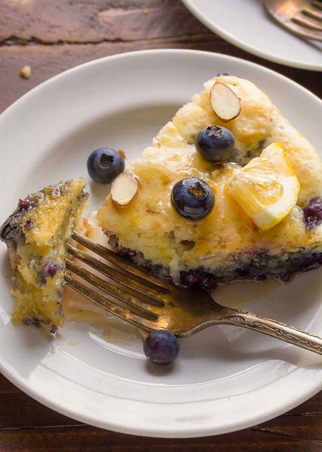 a slice of deep dish pancake with blueberries on a white plate with maple syri=up