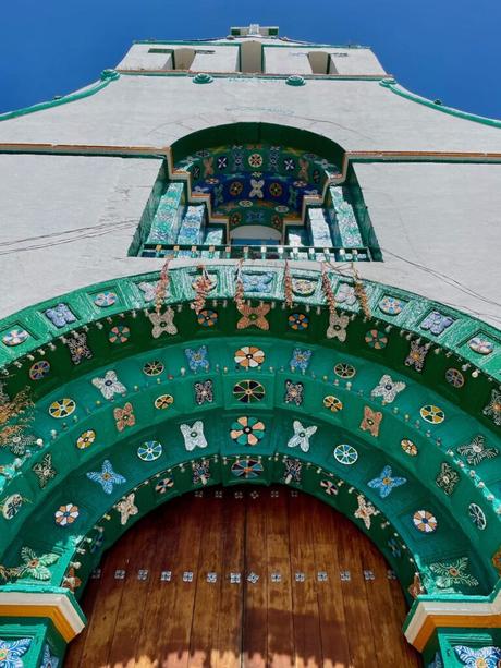 The ornate, colorful green and blue entrance arch of the church at Chamula, showing intricate patterns and wooden doors beneath a clear blue sky.