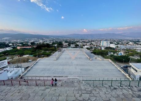 A panoramic view of the city of Tuxtla Gutierrez from a hilltop with wide, paved stairs leading down to an open plaza, and mountains on the horizon.