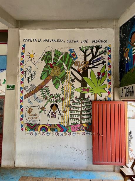 Colourful mural on the wall of a school room in Chiapas, with a bright orange door wide open on the right hand side.