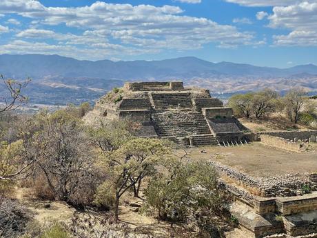 A close-up of a pyramid structure at Monte Albán, surrounded by trees and mountains under a clear blue sky.