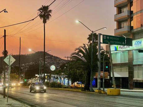 A city street at sunset with palm trees and traffic, with a sign pointing towards Mexico City and the Reforma neighborhood.