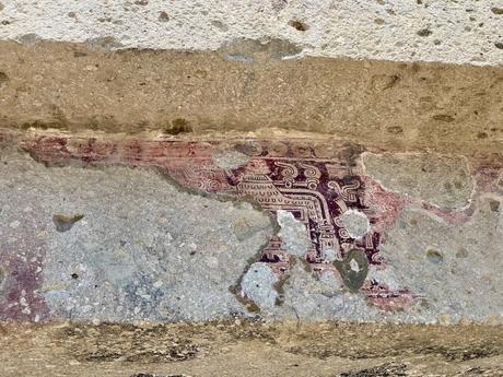 Faded, ancient red and white geometric murals painted on a stone wall, remnants of a pre-Columbian civilization.