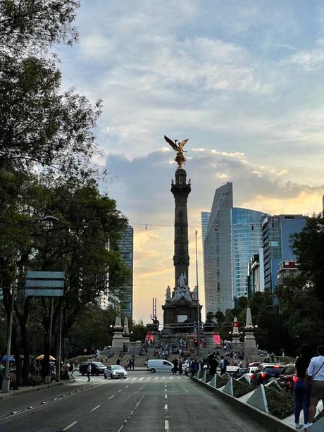 The Ángel de la Independencia (Angel of Independence) monument in Mexico City, standing tall on a column surrounded by buildings, with a vibrant sky in the background.