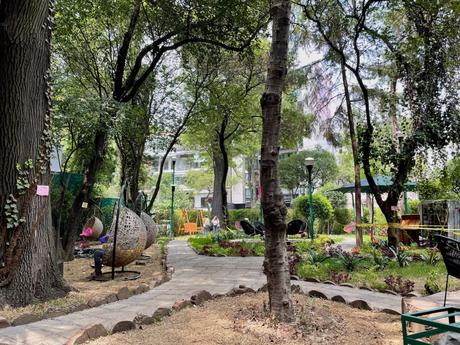 A peaceful park in La Condesa with trees and hanging chairs, surrounded by greenery and pathways, offering a quiet spot in a bustling city.