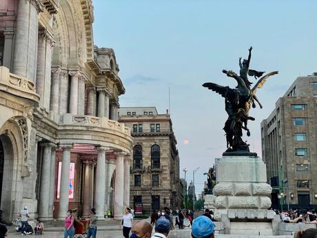 A close-up of the ornate architecture of Palacio de Bellas Artes, with a bronze statue of Pegasus in the foreground and a full moon visible in the distance.