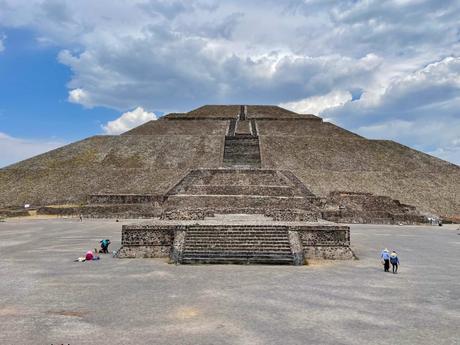 The Pyramid of the Sun at Teotihuacan, with its impressive stone steps and scattered visitors seen from the base under a partly cloudy sky.