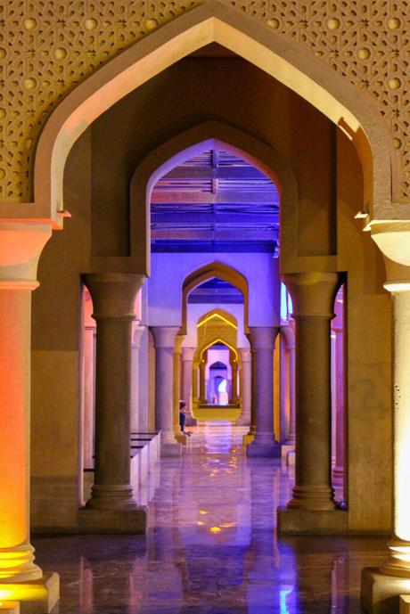 A hallway with a series of arches in Arabian architectural style, illuminated in different colored lights, creating a visually captivating corridor.