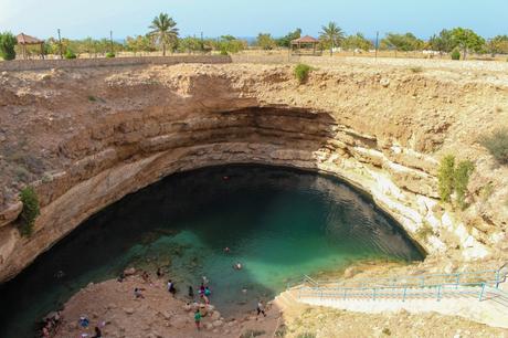 A natural sinkhole with turquoise waters, surrounded by rocky walls, with visitors swimming and enjoying the scene.