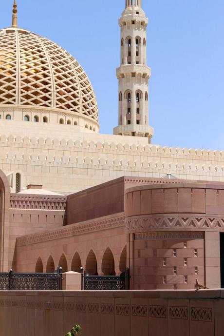 A detailed view of the dome and minaret of the Sultan Qaboos Grand Mosque, with intricate lattice designs and arched architecture.