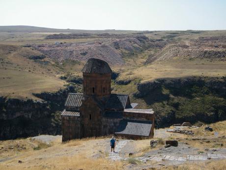 The Church of St. Gregory of Tigran Honents, a historic Armenian church situated on the edge of a canyon, with a lone visitor approaching the structure.