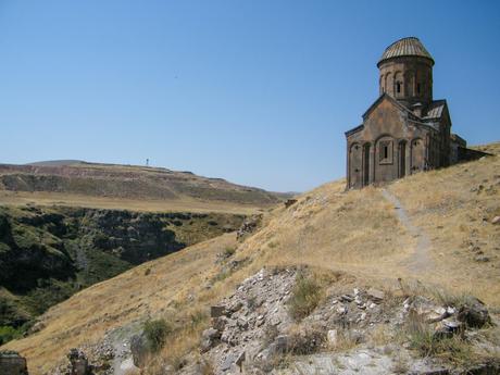 A lone, ancient church standing on a dry, rugged hilltop, with a vast barren landscape stretching into the distance under a clear blue sky.