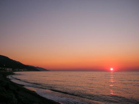 A breathtaking sunset over the sea, with the sun dipping below the horizon, casting a warm orange glow across the water and sky.