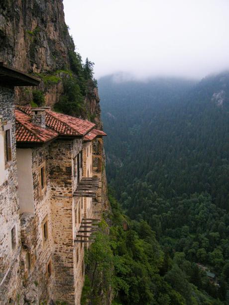 An ancient monastery built into a steep cliffside, surrounded by dense forest and shrouded in mist, showcasing its historic architecture.