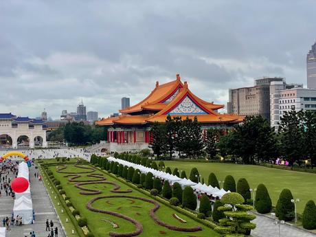 A different angle of the National Theater showing its intricate orange roof and decorative details, with a pathway lined by green hedges and white tents leading toward Liberty Square.