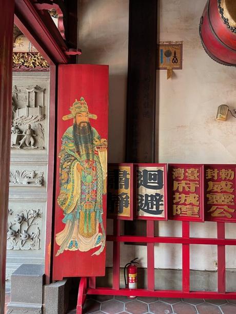 A wooden temple door painted with a detailed illustration of a historical figure in traditional attire, surrounded by Chinese calligraphy and ornate designs.