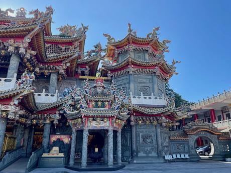 A beautifully detailed temple featuring colorful, intricate roof carvings of dragons and mythical creatures under a bright sky.