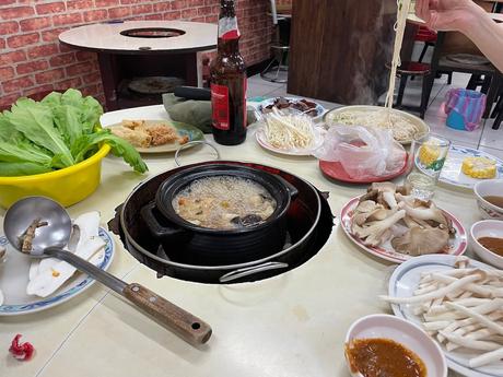 A bubbling hot pot surrounded by various fresh ingredients such as mushrooms, lettuce, and noodles, with plates and sauces ready for cooking.