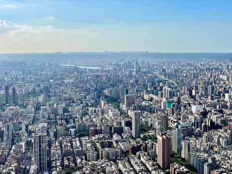 A sprawling aerial view of Taipei city showcasing densely packed buildings, highways, and rivers under a clear, bright sky.