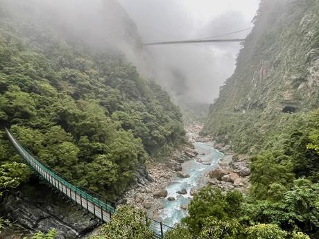 Two suspension bridges spanning across Taroko Gorge, surrounded by lush greenery and misty mountains.