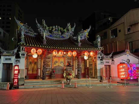 An illuminated traditional temple at night in Tainan, adorned with glowing red lanterns and intricate carvings, creating a warm and festive atmosphere.