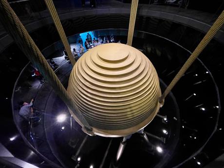 The massive golden damper inside Taipei 101, used for structural stability, surrounded by ropes and reflections of spectators below.