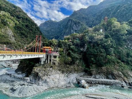 A bright red suspension bridge leading to a pagoda nestled in the green mountains of Taroko Gorge.