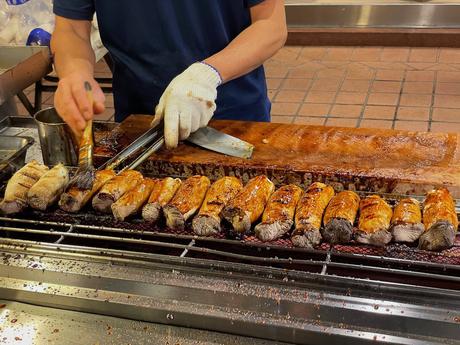 A vendor grilling skewered mushrooms brushed with sauce, creating a row of golden, caramelized skewers.