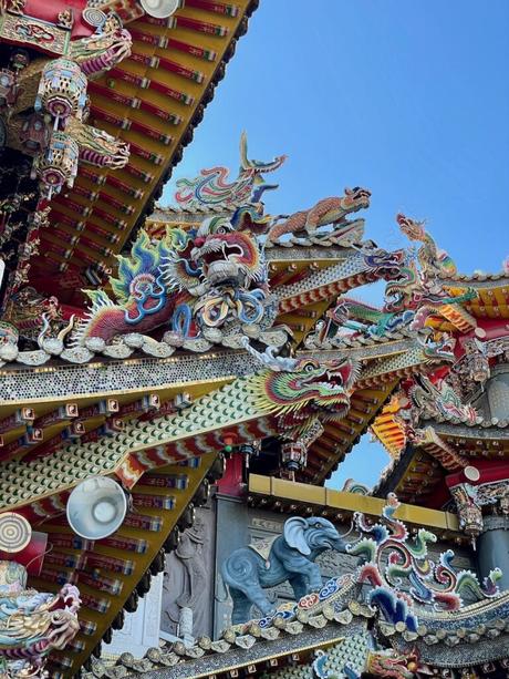 Elaborate carvings on a temple roof, showcasing a vibrant dragon and other mythical creatures in vivid colors and fine detail.