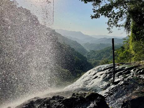 A close-up view of sunlight sparkling through water droplets from a waterfall, with a distant mountain landscape in the background.