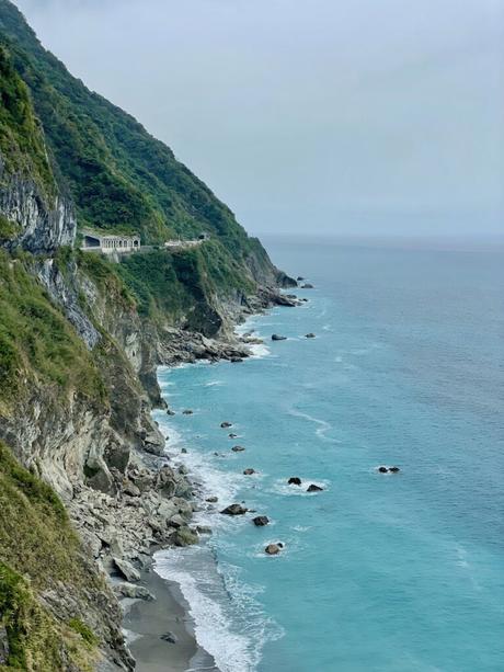 A rocky coastline with dramatic cliffs extending into the distance, featuring turquoise waters and scattered rocks along the shore.