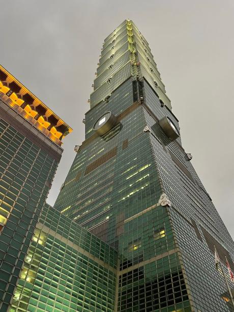 A close-up view of the Taipei 101 skyscraper against a moody gray sky, showcasing its green-tinted glass exterior and unique design details.