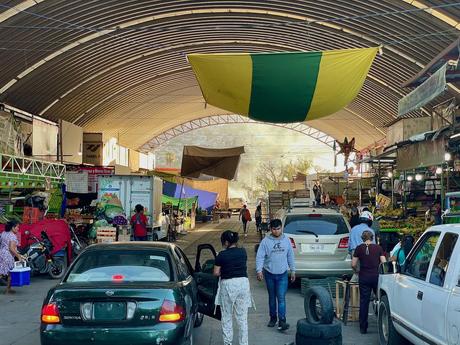 Outside the entrance of the Mercado de Abastos in Oaxaca with market vendors and cars underneath a large metal arched roof