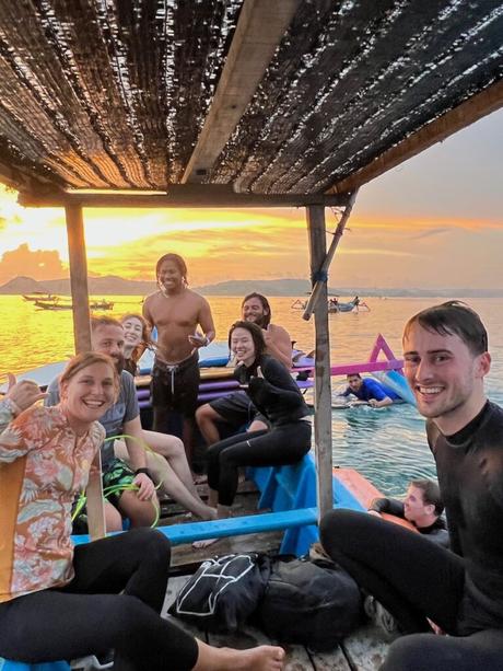 A group of smiling people in a small boat after surfing at Gerupuk Lombok at sunset