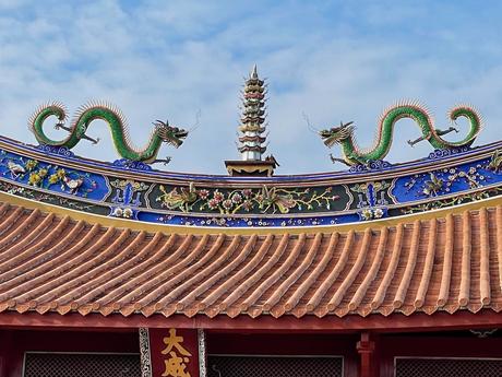 A detailed view of a traditional Taiwanese temple roof adorned with green ceramic dragons, intricate floral motifs, and a central spire, set against a blue sky.