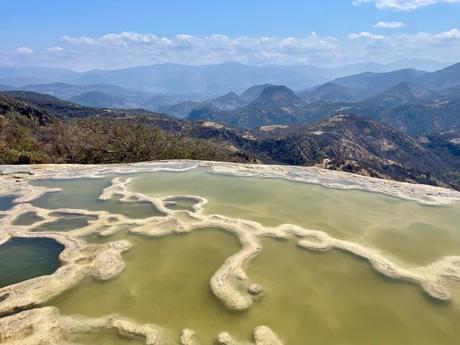 A panoramic view of the petrified waterfalls and natural pools at Hierve el Agua, with mountains stretching into the distance under a clear sky.