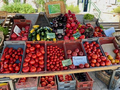 A colorful display of fresh red tomatoes, bell peppers, and zucchinis neatly arranged in crates at a local farmers' market.