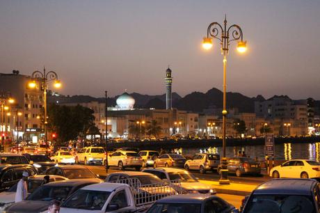 19 Best Places to Visit in Oman A cityscape of Muscat, Oman, at dusk, with cars filling the streets, and a mosque with a domed roof and minaret lit up against the backdrop of mountains.
