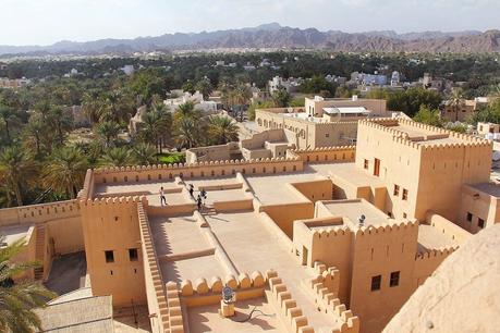 19 Best Places to Visit in Oman View from the top of the fort in Nizwa Oman with palm trees surrounding the city and rocky mountains beyond