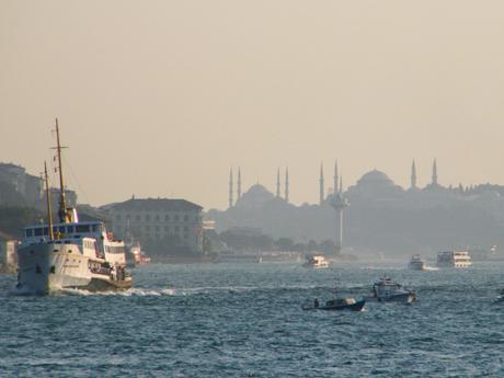 20 Best Places to Visit in Turkey Boats sailing in the Bosphorus with a hazy view of Istanbul in the background, featuring the silhouette of famous mosques with their minarets piercing the sky.