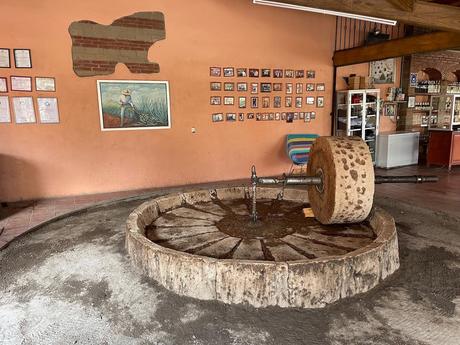 19 Best Places to Visit in Oaxaca State Traditional horse-drawn stone grinder wheel used for pulverising agave as part of the mezcal production process at a mezcal producer in Oaxaca. Behind the orange wall has several photos and other information showing the process of producing mezcal in Oaxaca