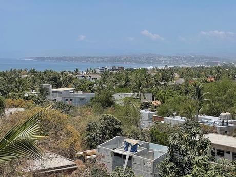 19 Best Places to Visit in Oaxaca State Wide open view of Puerto Escondido with low-rise rooftops sticking out of the greenery and the curved bay of Playa Zicatela beyond