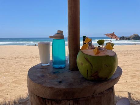 19 Best Places to Visit in Oaxaca State Drinks and a coconut on a wooden table at a beach bar on the Oaxaca coast
