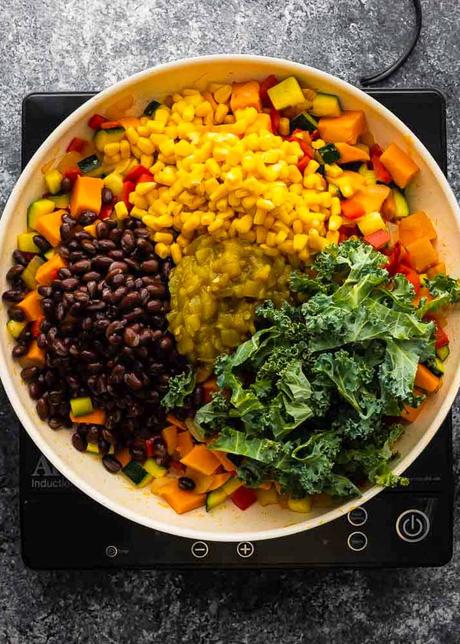 Vegetarian Enchiladas cooked vegetables, black beans, corn and kale in a large skillet